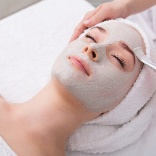 Face peeling mask, spa beauty treatment, skincare. Woman getting facial care by beautician at spa salon, side view, close-up